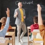 Teacher interacting with students raising hands in a classroom setting.