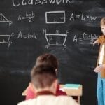 A young student explains math formulas on a blackboard during classwork.