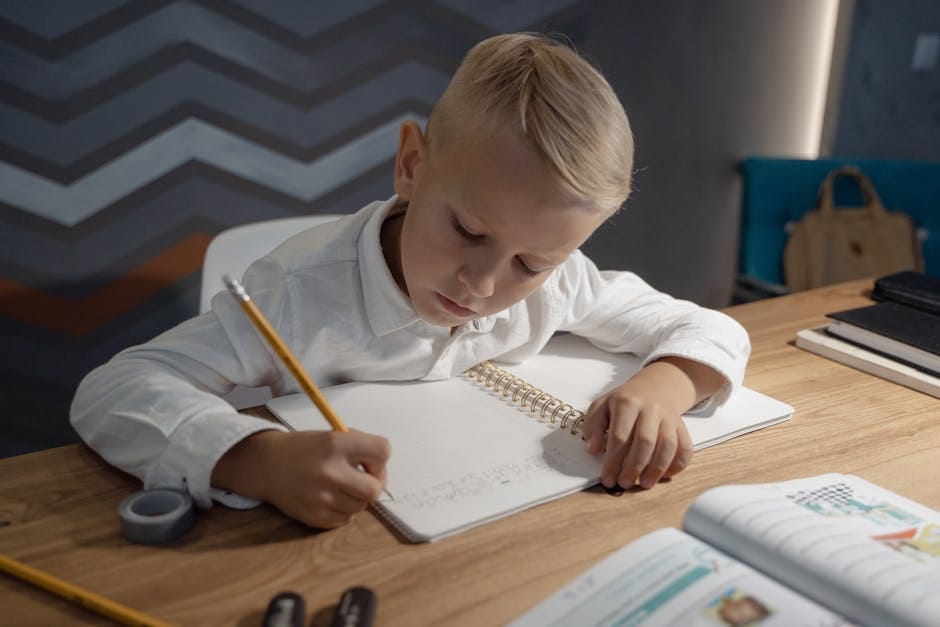 A young boy diligently writing homework in a notebook at a wooden desk indoors.