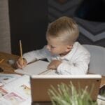 A young boy focuses on homework with books and a tablet at a desk, enhancing his education.