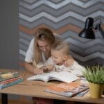 A mother assists her son with homework at a desk, fostering a learning environment.