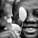 Close-up of a smiling child holding a leaf, captured in monochrome for an artistic touch.