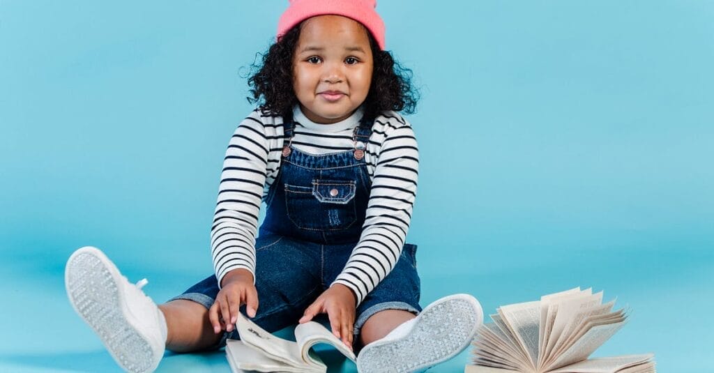 A cute African American girl reading books on a vibrant blue background, full of curiosity and delight.