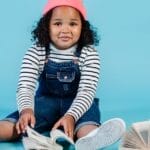 A cute African American girl reading books on a vibrant blue background, full of curiosity and delight.