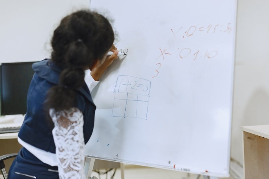 A student writes mathematical equations on a whiteboard in a classroom setting.