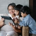 An Asian grandmother spending quality time with her grandchildren, sharing a moment on a tablet.