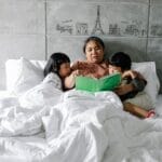 A grandmother reads a storybook to her grandchildren, creating a cozy moment in a bedroom.