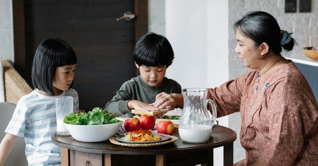 Grandmother sharing a meal with two children at a table full of fresh food indoors.