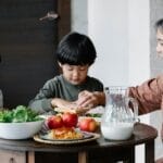 Grandmother sharing a meal with two children at a table full of fresh food indoors.