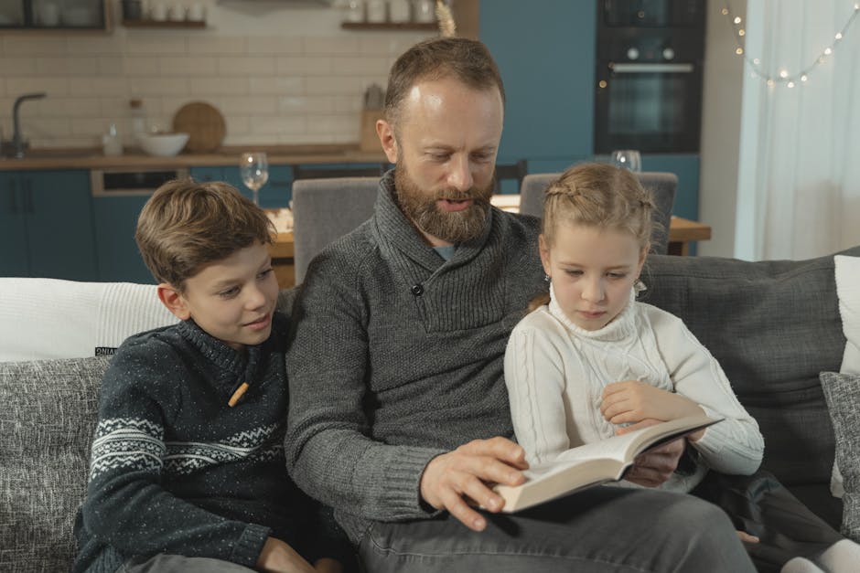 A father reading a book with his two children on a sofa in a warm indoor setting.