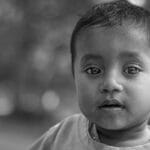 Close-up black and white portrait of a young boy with expressive eyes in soft focus.