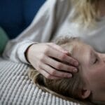 A child peacefully resting while a caregiver gently holds their head in a comforting gesture.