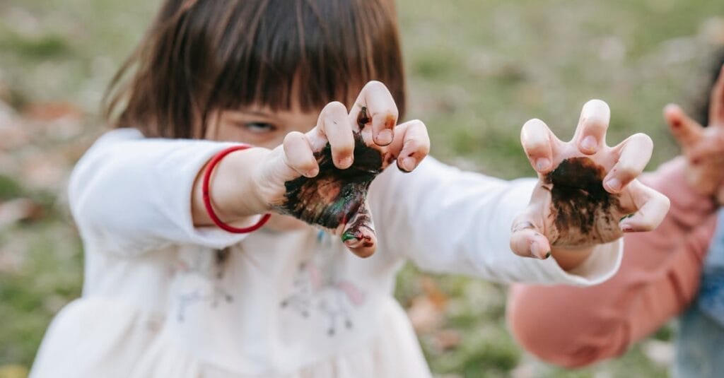 Crop girl demonstrating scary face while frightening with dirty hands during Halloween celebration in nature