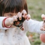 Crop girl demonstrating scary face while frightening with dirty hands during Halloween celebration in nature