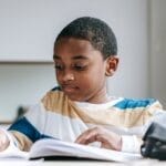 Young boy attentively studying with open notebook and pencil indoors.