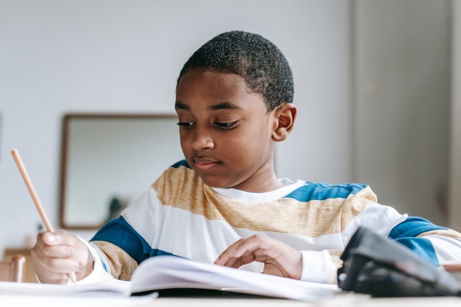 Young boy attentively studying with open notebook and pencil indoors.