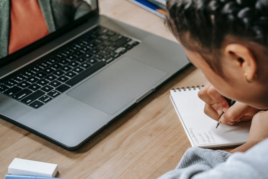 Child engaged in online education using a laptop and taking notes in a notebook.