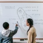 Two kids learning biology, engaging with a whiteboard diagram of a paramecium in a classroom setting.