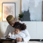 Father and daughter bonding while reading a book indoors, enjoying quality time.