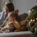 Cozy moment of mother and daughter reading together by a Christmas tree.