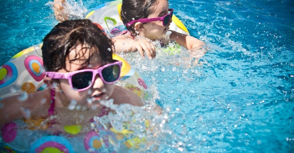 Two young girls enjoying a playful day in a bright blue swimming pool with colorful float rings.