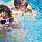 Two young girls enjoying a playful day in a bright blue swimming pool with colorful float rings.