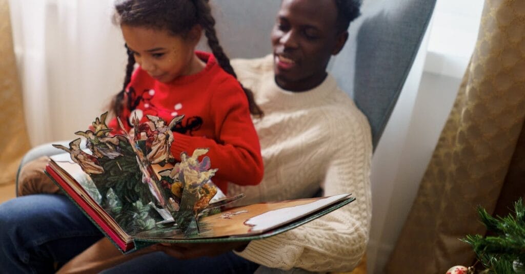 A father bonding with his daughter during Christmas by reading a pop-up book together at home.