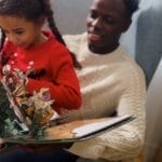 A father bonding with his daughter during Christmas by reading a pop-up book together at home.