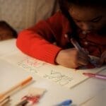 Young girl writing a letter to Santa Claus with colorful pens indoors, capturing holiday spirit.