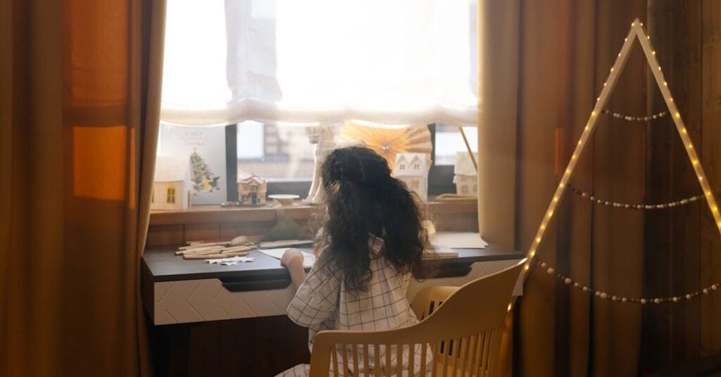 A young girl creatively drawing holiday cards indoors with festive decorations around her.
