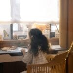 A young girl creatively drawing holiday cards indoors with festive decorations around her.