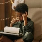 A young child intensely focused on drawing while sitting indoors in a cozy and warm setting.