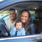 A joyful family with a baby in a car, expressing happiness and togetherness.