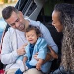 A joyful family moment captured inside a car trunk with parents and their toddler laughing.