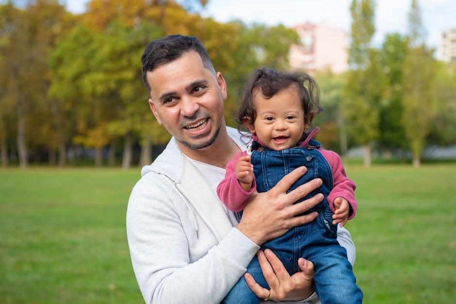 A loving father holds his joyful child with Down syndrome in a park, surrounded by greenery.