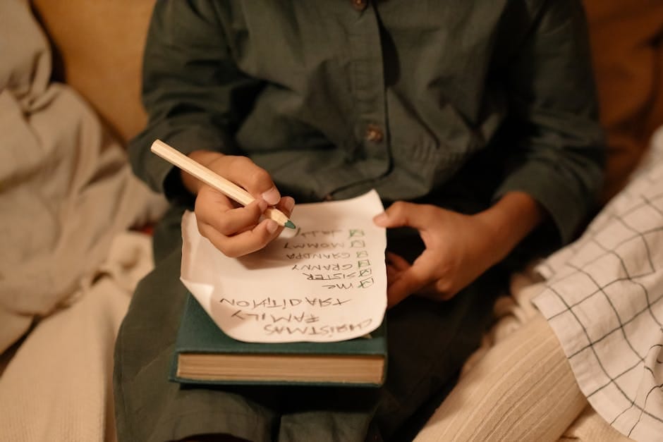 A child writes a Christmas wish list with green pencil on cozy winter evening. Family tradition and holiday joy.