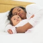 A mother and her baby with Down syndrome sleeping together in bed.