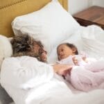 A mother and child with Down syndrome share a tender moment on a cozy bed, emphasizing family love.