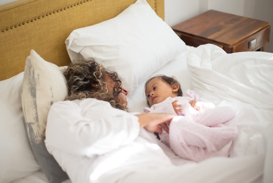 A mother and child with Down syndrome share a tender moment on a cozy bed, emphasizing family love.