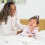 A joyful mother and her baby spending quality time on a cozy bed indoors.