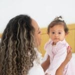 A loving mother holds her baby daughter in a cozy bedroom setting.