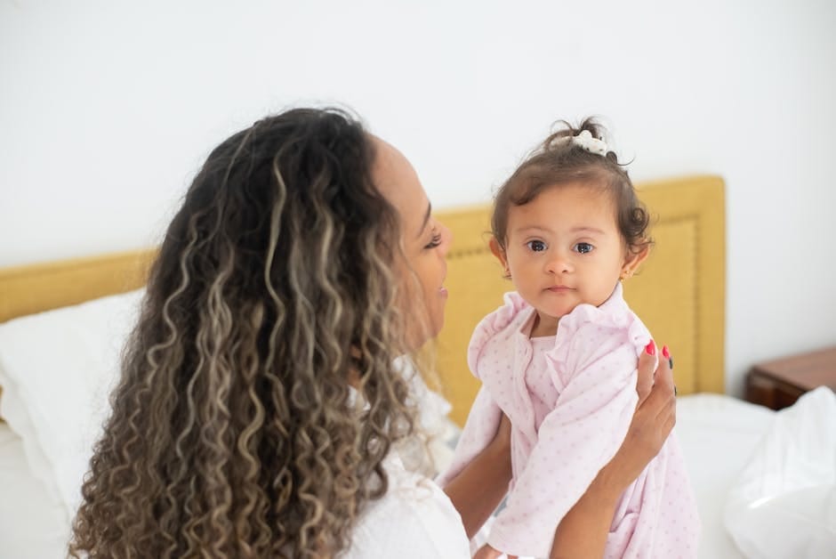 A loving mother holds her baby daughter in a cozy bedroom setting.