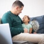 A father spending quality time with his daughter on a comfortable sofa at home.