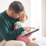 A tender moment as a father reads a book to his young daughter at home.