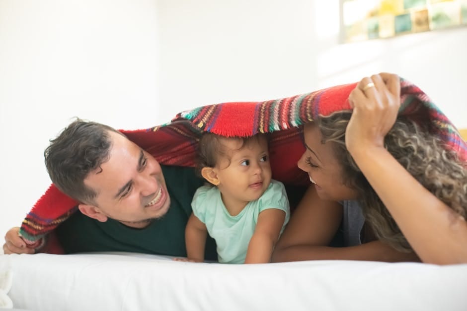 Joyful family of three sharing loving moments under a blanket indoors.