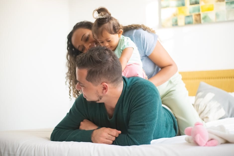 A cheerful family enjoys playful bonding time together indoors in a bright, cozy bedroom.