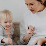 A mother and her toddler daughter draw together, sharing a heartwarming moment indoors.