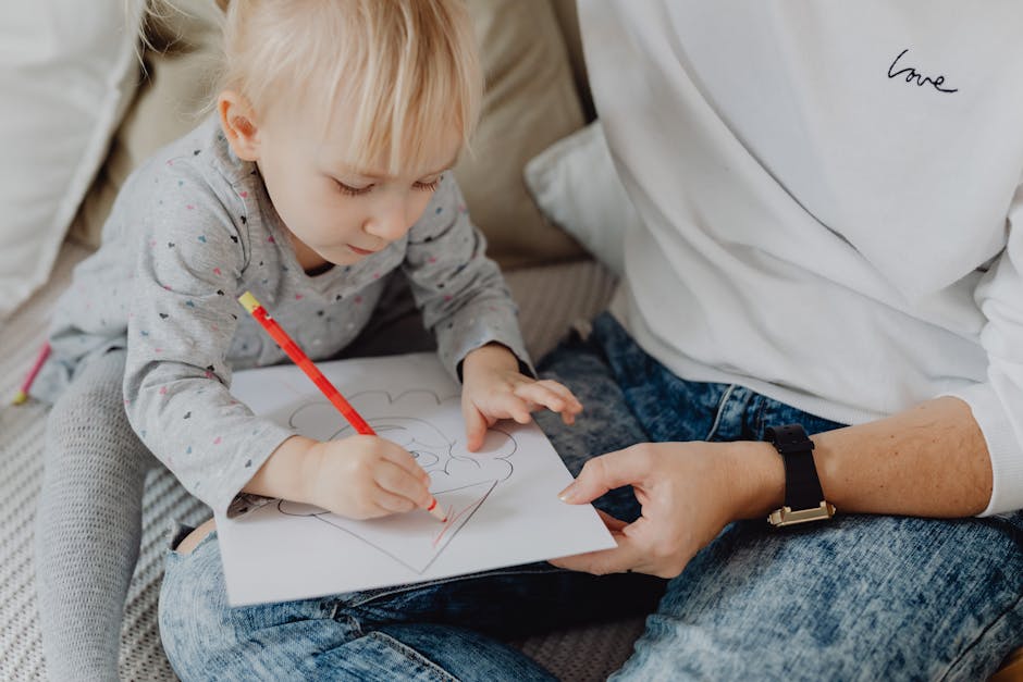 Young child focused on coloring paper with a red pencil, aided by an adult.