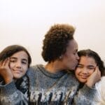 A joyful mother kissing her smiling daughters indoors, capturing love and family warmth.