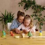 A mother and daughter enjoying creative playtime with wooden toys at the table indoors.